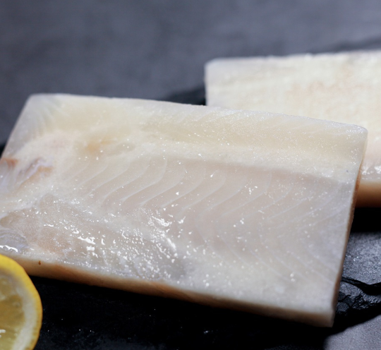 Raw frozen dory steak displayed on a black marble plate